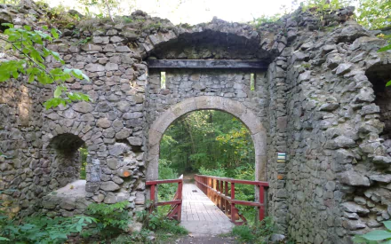 View through the stone ruins of Cisy Castle, featuring an arched gateway and a wooden bridge surrounded by lush greenery in this HD desktop wallpaper.