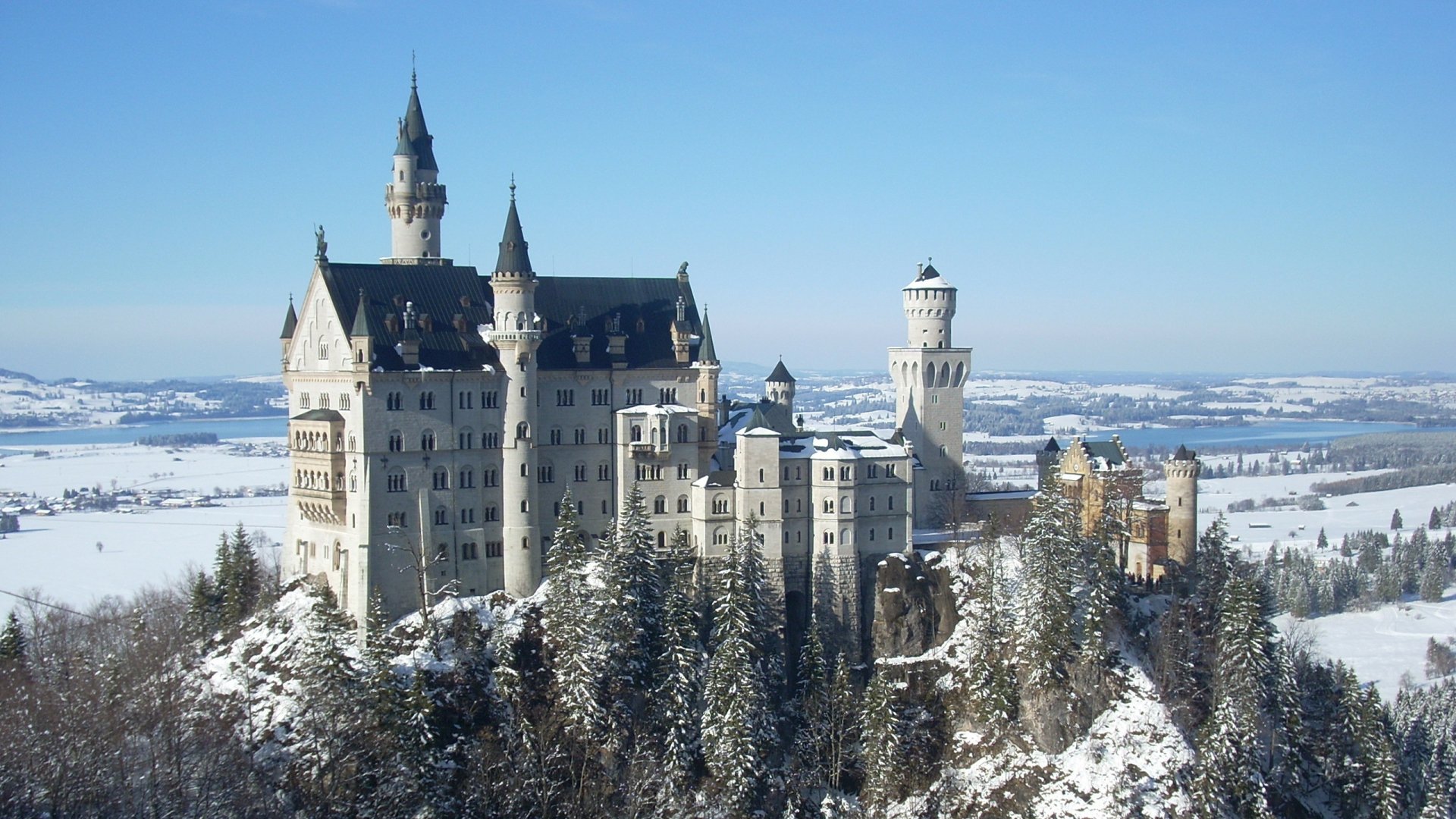 HD desktop wallpaper featuring the man-made Neuschwanstein Castle perched on a snowy hill with a clear blue sky in the background.