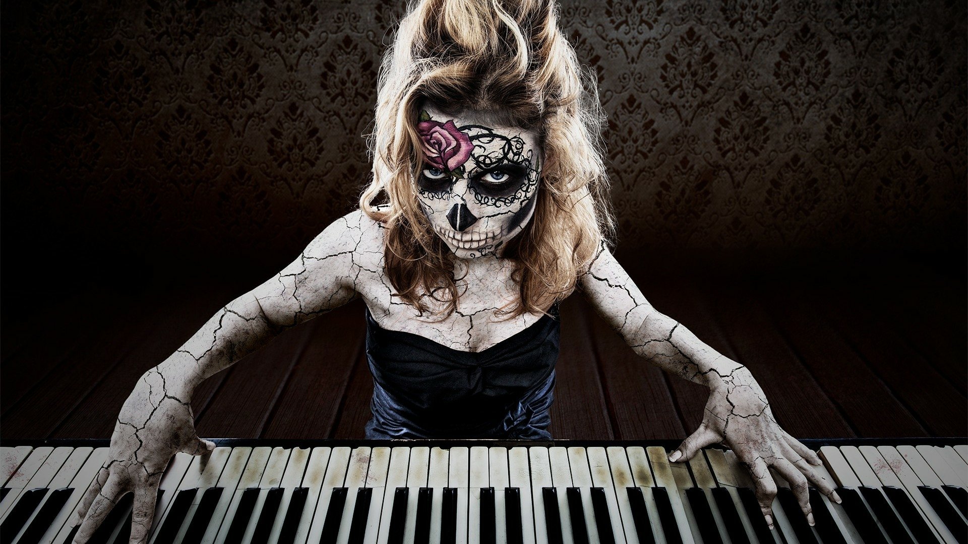 Artistic HD PC desktop wallpaper featuring a woman with detailed sugar skull face paint and cracked body art playing piano against a dark, textured background.