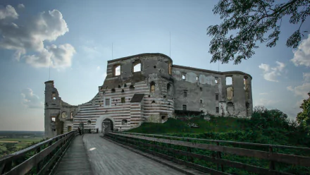 Man-made Janowiec Castle ruins on a wooden approach bridge beneath dramatic clouds — 2K Quad HD PC desktop wallpaper and background.