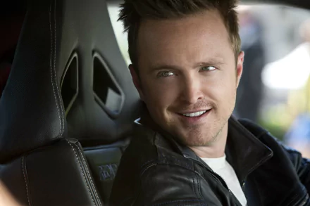 Aaron Paul smiles while seated in a car, capturing a moment from the movie Need For Speed. This HD wallpaper showcases his captivating presence.
