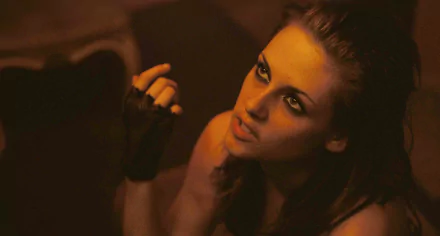 Cinematic close-up of a young woman with smoky eye makeup reaching upward in warm, dim light — movie Welcome to the Rileys, 2K Quad HD PC desktop wallpaper/background.