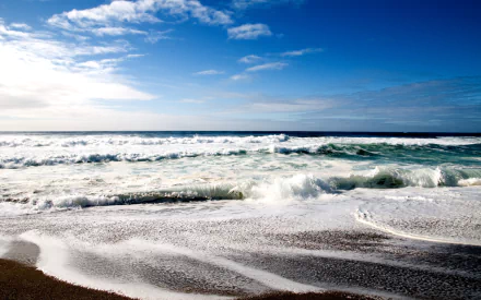 HD PC desktop wallpaper featuring a vibrant seascape with waves crashing onto a sandy shore under a bright blue sky with scattered clouds.