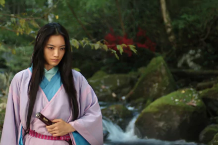 HD PC desktop wallpaper from the movie Shinobi: Heart Under Blade — a female shinobi in a pink kimono clutching a sheathed blade beside a mossy forest stream.