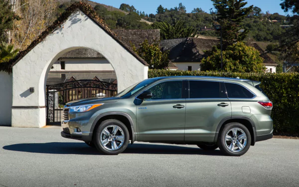 HD desktop wallpaper featuring a Toyota Highlander Hybrid parked in front of a white arched gate with greenery and cottages in the background.