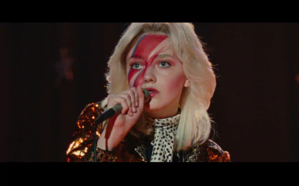 HD PC desktop wallpaper: blonde actress in glam-rock look with a red lightning-bolt face paint, singing into a microphone in a scene from the movie The Runaways.