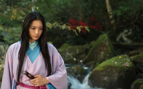HD PC desktop wallpaper from the movie Shinobi: Heart Under Blade — a female shinobi in a pink kimono clutching a sheathed blade beside a mossy forest stream.