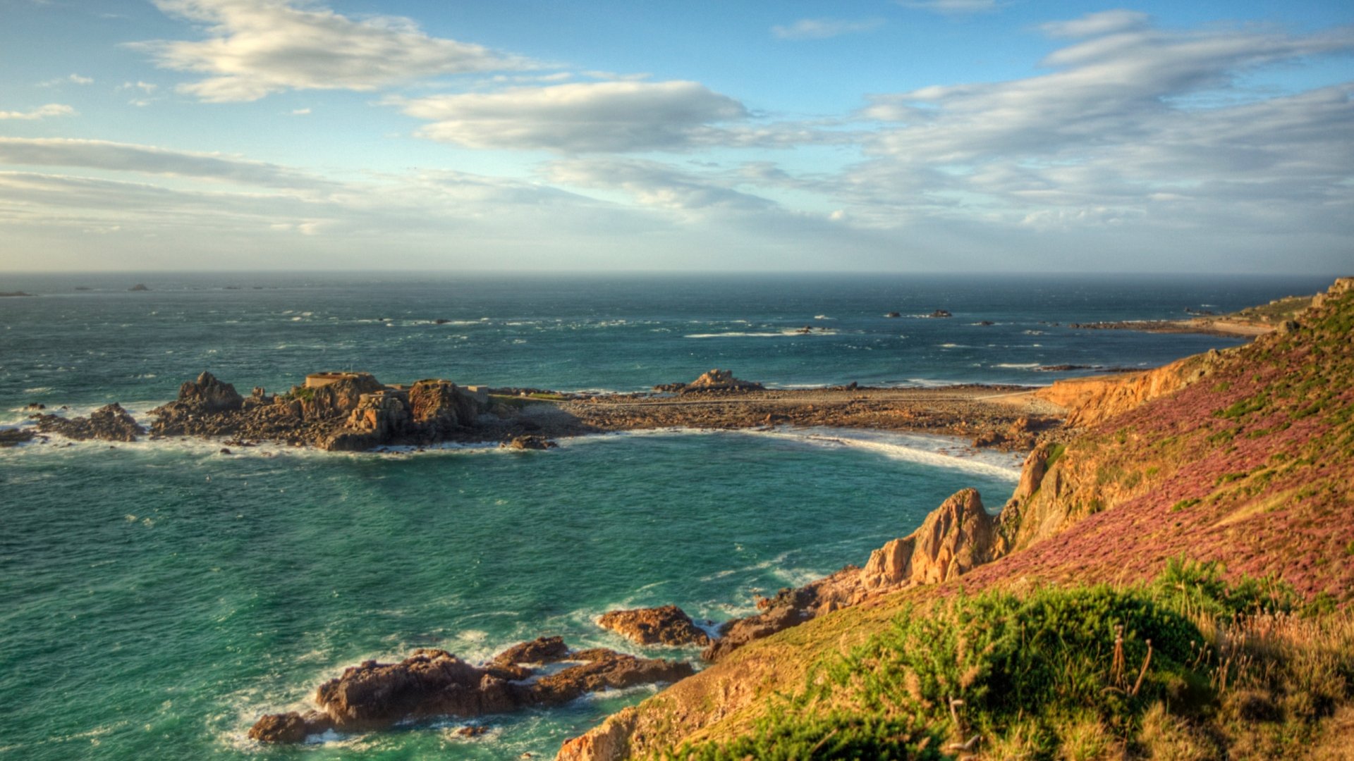 HD desktop wallpaper showcasing the man-made Fort Clonque overlooking a rugged coastline with turquoise waters and partly cloudy skies.