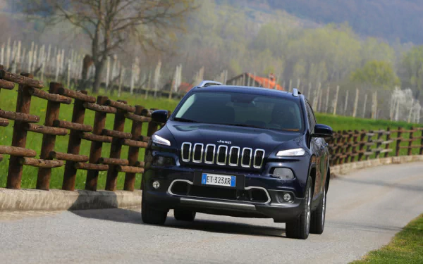HD PC desktop wallpaper and background: vehicle — dark Jeep Cherokee driving along a tree-lined country road beside wooden fences.
