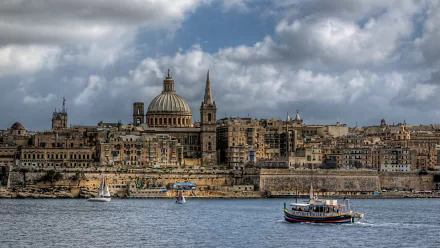 HD desktop wallpaper featuring the man-made skyline of Valletta with historic buildings and boats on calm water under a partly cloudy sky.
