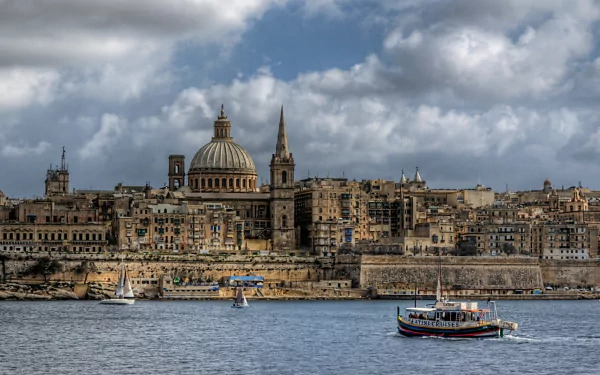 HD desktop wallpaper featuring the man-made skyline of Valletta with historic buildings and boats on calm water under a partly cloudy sky.