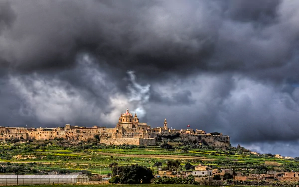 HD desktop wallpaper featuring the man-made historic cityscape of Mdina under a dramatic, stormy sky.