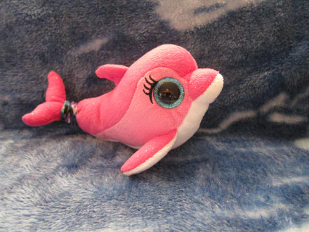 A bright pink Beanie Boos plush dolphin with large blue eyes resting on a soft dark blue fabric, shown as an HD PC desktop wallpaper and background.