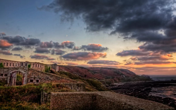 HD PC desktop wallpaper of Fort Tourgis, a man-made coastal fortification bathed in the warm light of a dramatic sunset under a partly cloudy sky.