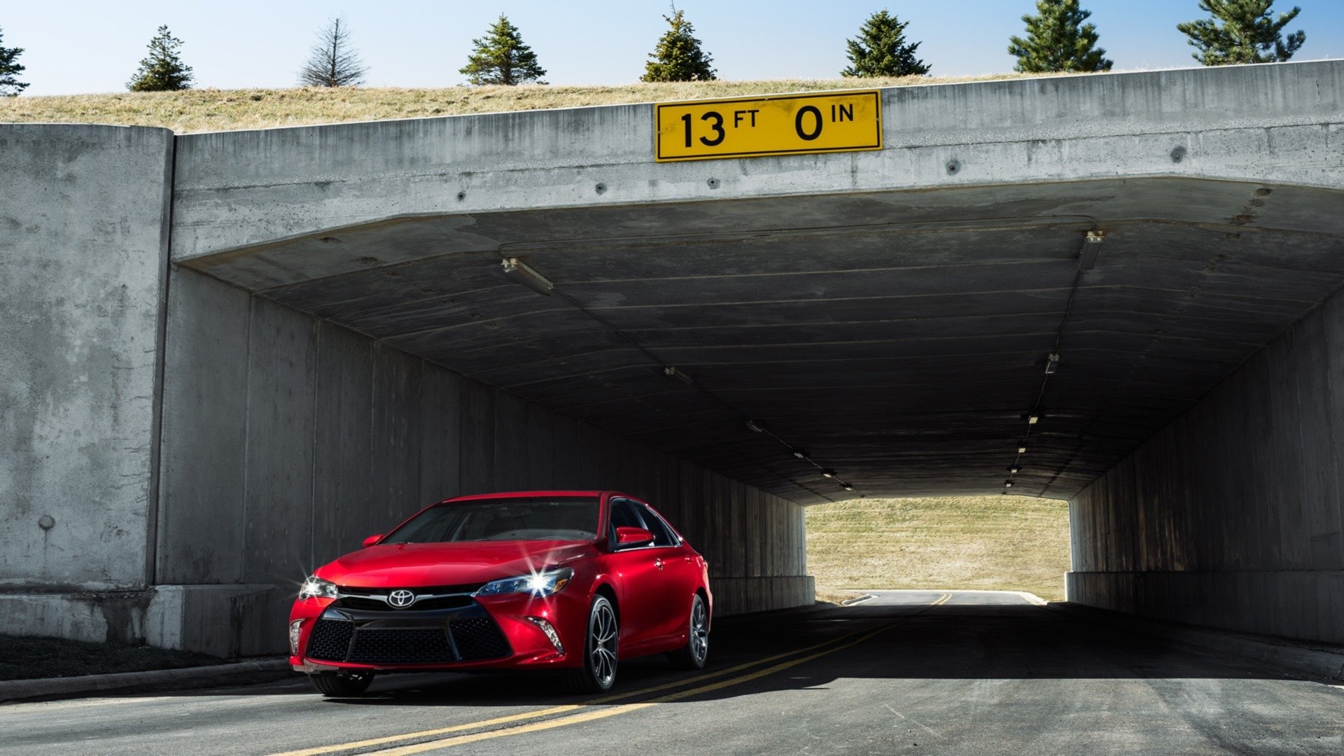 HD PC desktop wallpaper background showing a red 2015 Toyota Camry vehicle in a concrete underpass, sunlight ahead and a 13 ft clearance sign overhead.