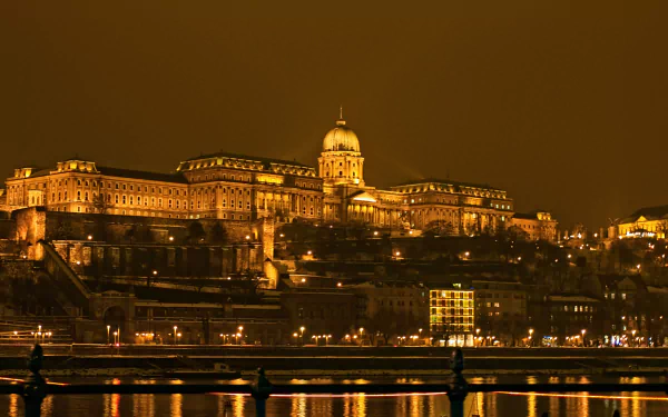 Night view of the illuminated Buda Castle, a man-made historic landmark, reflected in the calm river, captured in HD for a stunning desktop wallpaper.
