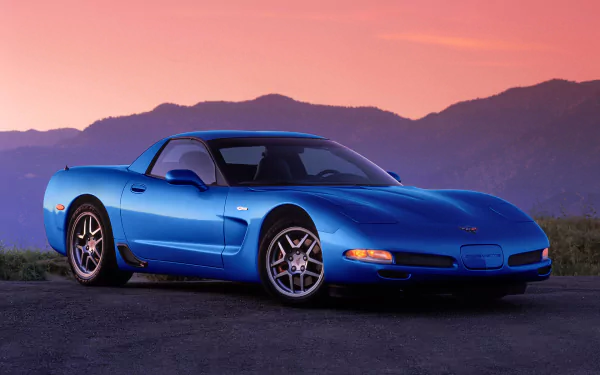 A blue Chevrolet Corvette Z06 parked on a road with mountains and a pink-orange sunset sky in the background, shown as an HD PC desktop wallpaper.