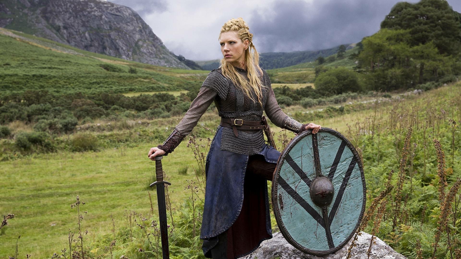 HD desktop wallpaper featuring Lagertha, portrayed by Katheryn Winnick, from the TV show Vikings (2013), standing in a scenic mountainous landscape with sword and shield.