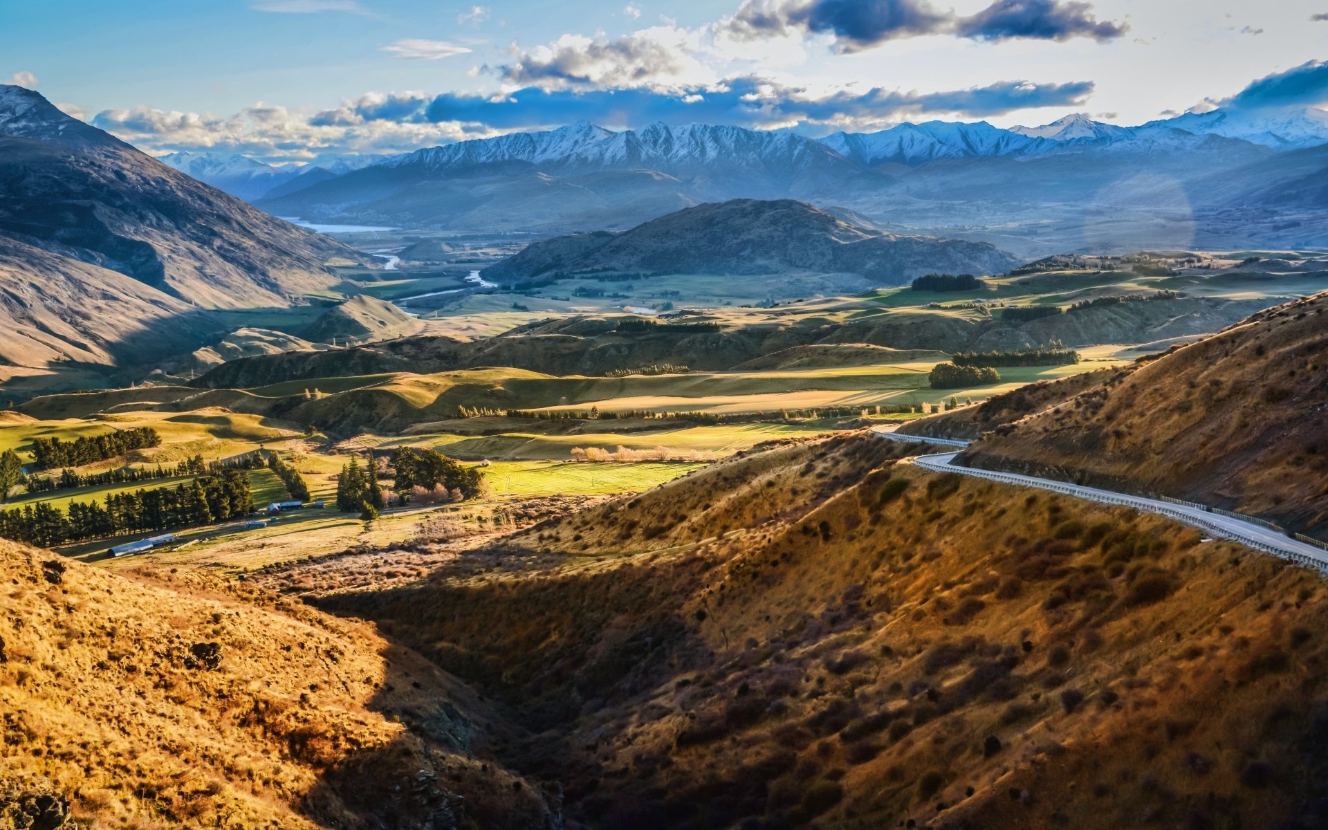 Nature landscape: sunlit valley with winding road, patchwork fields and distant snow-capped mountains — HD PC desktop wallpaper and background.