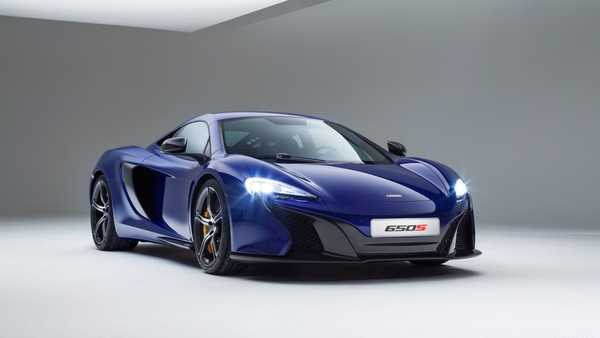 Blue McLaren 650S supercar pictured in a clean studio, sleek lines and lit headlights — HD PC desktop wallpaper and vehicle background.
