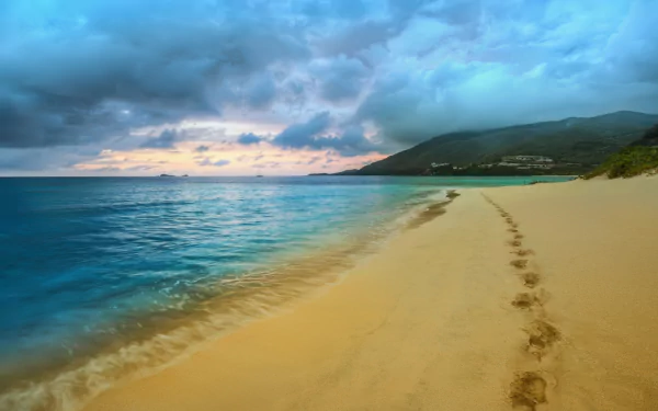 HD desktop wallpaper showcasing a serene seascape with a cloudy sky, gentle waves, a sandy beach with footprints, and a coastal landscape in natural beauty.