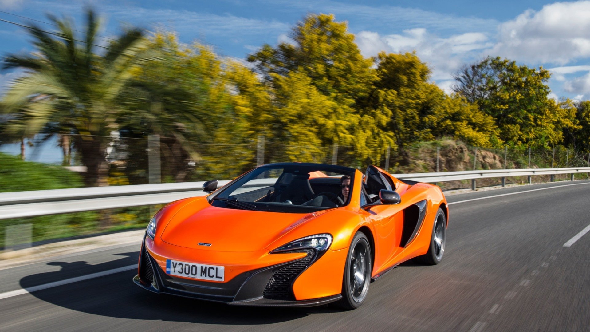 Orange McLaren 650S Spider supercar driving along a coastal road — HD PC desktop wallpaper and background.