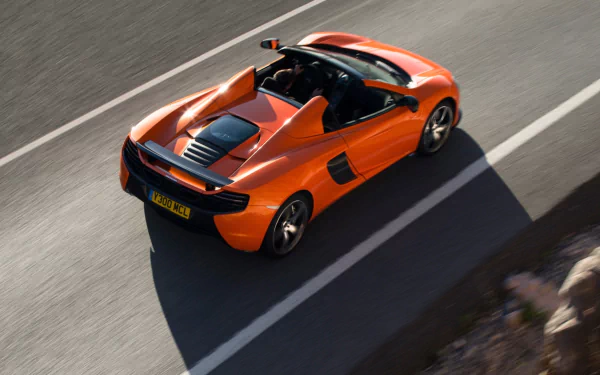 Orange McLaren 650S Spider supercar speeding on a road, captured in high-definition for a dynamic PC desktop wallpaper and background.