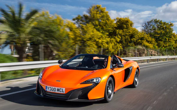 Orange McLaren 650S Spider supercar driving along a coastal road — HD PC desktop wallpaper and background.