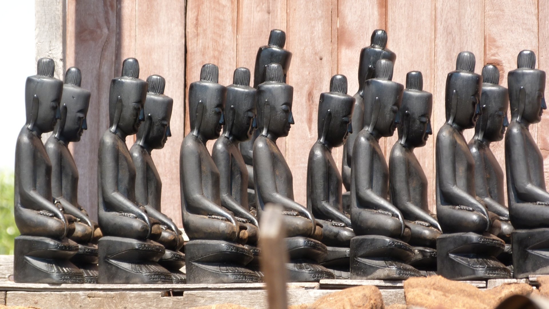 Row of black Buddha statues arranged in meditation pose against a wooden background, captured in an HD desktop wallpaper reflecting Buddhist religious art.