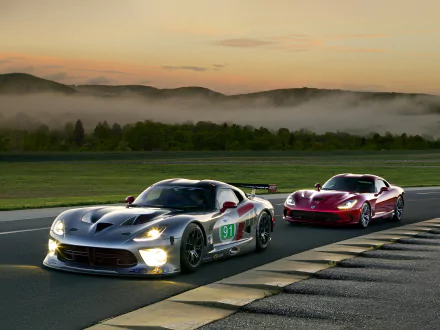 HD PC desktop wallpaper showing two Dodge Viper vehicles on a racetrack at dawn — a silver Dodge Viper GTS-R leading a red Viper with misty hills in the background.
