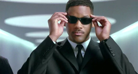 HD PC desktop wallpaper featuring a scene from the movie Men In Black with a man adjusting his sunglasses in a sleek black suit.