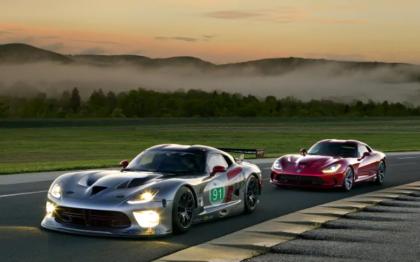 HD PC desktop wallpaper showing two Dodge Viper vehicles on a racetrack at dawn — a silver Dodge Viper GTS-R leading a red Viper with misty hills in the background.