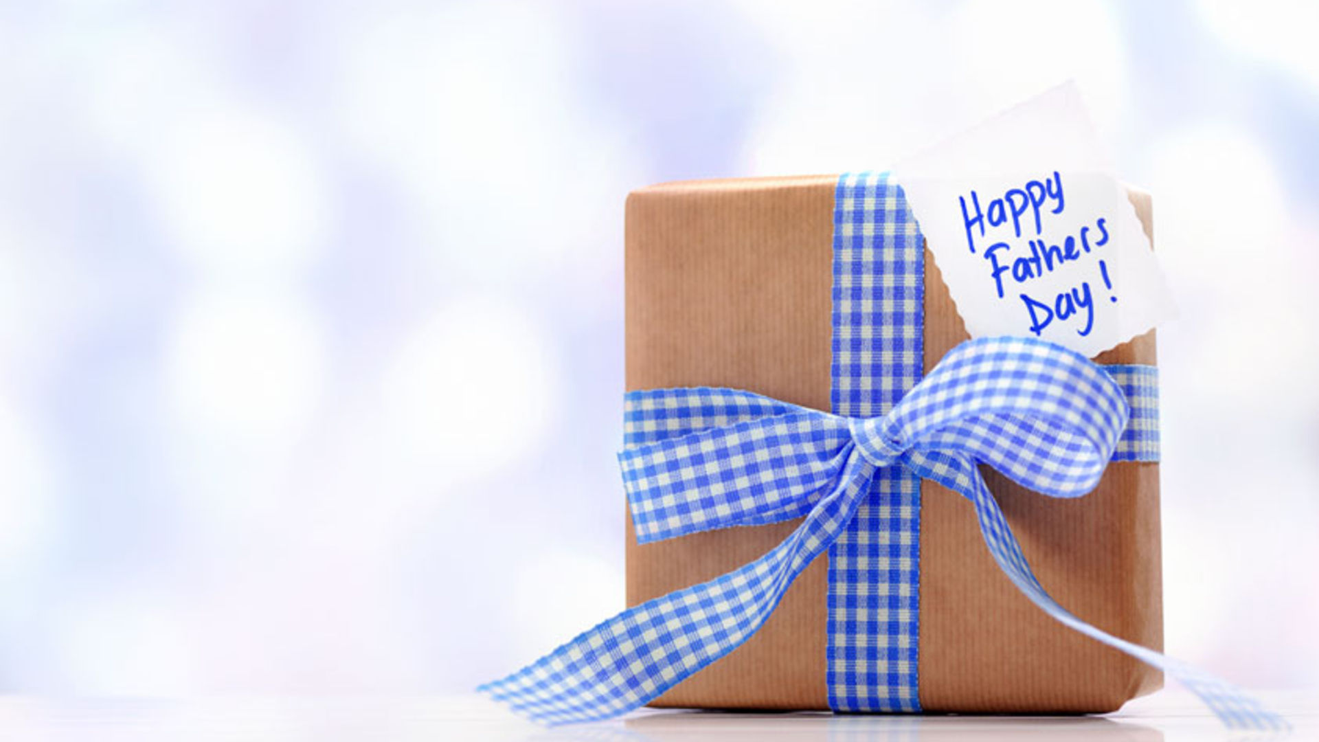 Father's Day themed HD desktop wallpaper with a gift wrapped in brown paper and a blue checkered ribbon, tag reading Happy Father's Day!