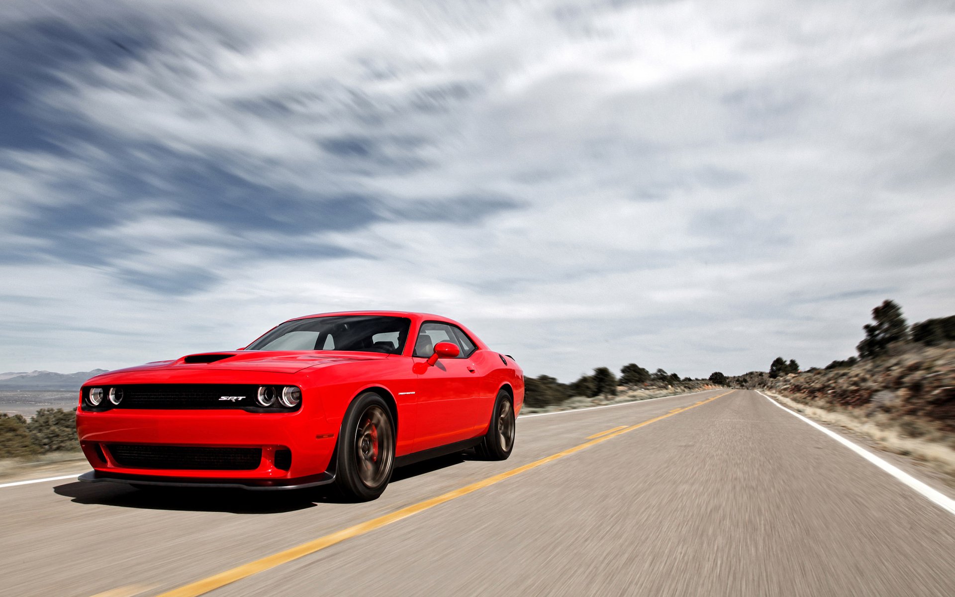 A vibrant red Dodge Challenger SRT Hellcat races down an open road under a partly cloudy sky. The image serves as a high-definition desktop wallpaper and background.