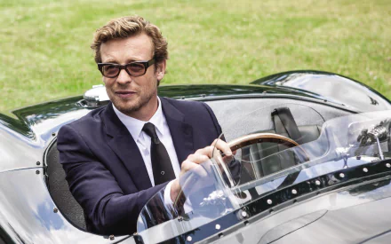 Australian actor and celebrity Simon Baker dressed in a suit, sitting in a classic convertible car, captured in an HD PC desktop wallpaper background.