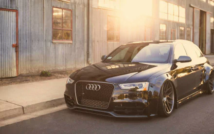 A sleek black Audi A4 parked beside a rustic building, bathed in warm sunlight, creating a striking HD desktop wallpaper and background.