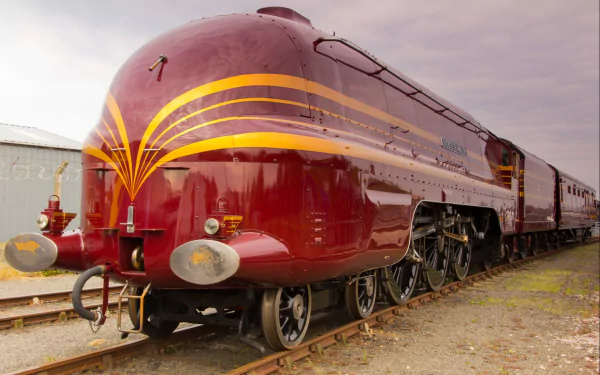 HD wallpaper featuring a striking maroon train with golden stripes, parked on railroad tracks under a cloudy sky.