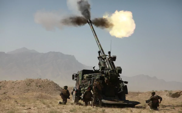 HD PC desktop wallpaper: CAESAR self-propelled artillery firing in a desert, soldiers nearby, muzzle flash and smoke with distant mountains in the background.