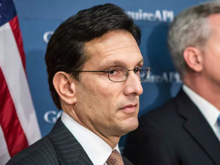 HD desktop wallpaper of a man in a suit with glasses looking to the side with an American flag in the background.