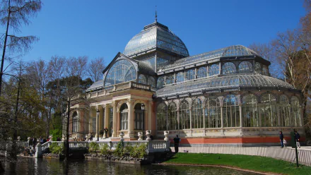 Man-made Palacio de Cristal glass pavilion beside a reflective pond under a clear blue sky — HD PC desktop wallpaper and background.