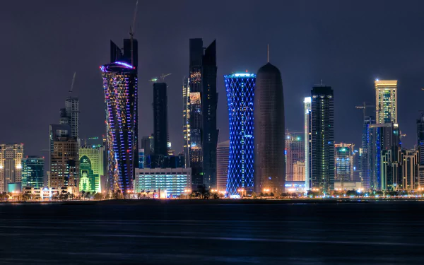 HD desktop wallpaper of Doha's skyline at night, featuring illuminated, man-made skyscrapers against a dark sky, reflecting vibrant colors.