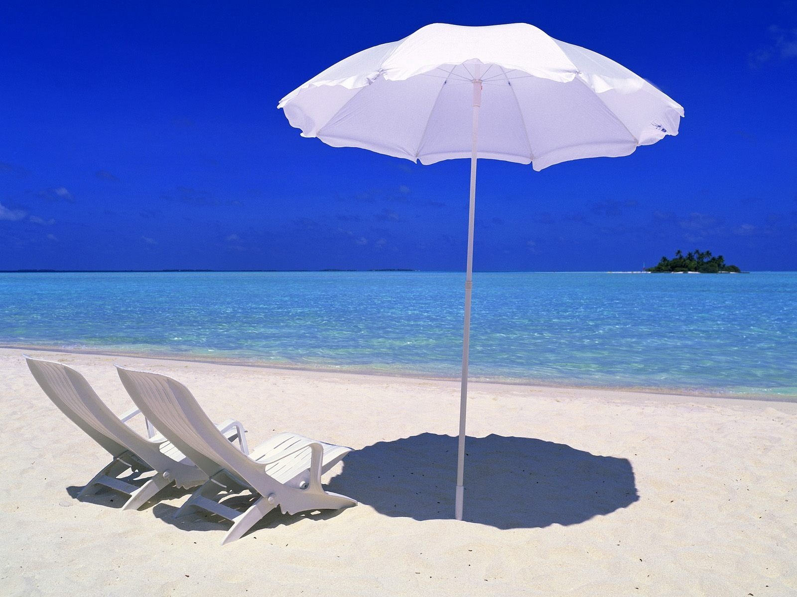 HD photography of a serene beach scene featuring two lounge chairs under a white umbrella with clear blue skies and a distant island, designed as a desktop wallpaper.