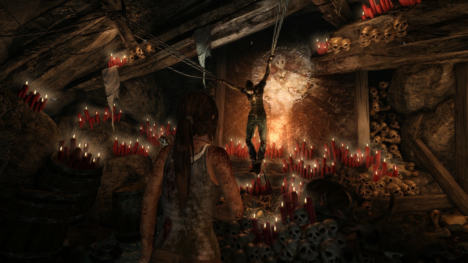 HD PC wallpaper from Tomb Raider (2013) featuring a dimly lit cavern with red candles, skulls, and a suspended figure, creating an intense and eerie atmosphere.