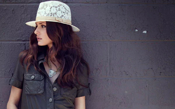 A stylish woman wearing a white hat and a green shirt poses against a textured gray wall, exuding confidence. This HD image showcases Olivia Palermo's chic vibe as a desktop wallpaper.