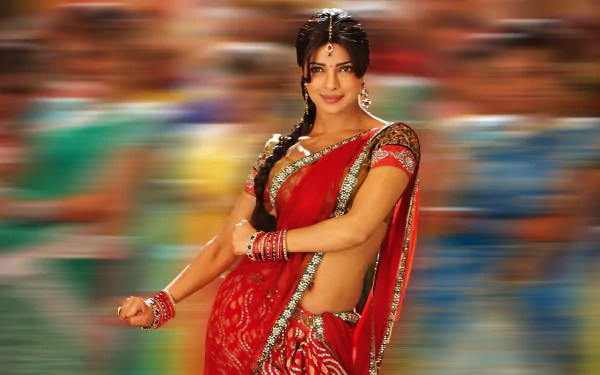 Priyanka Chopra shines in a vibrant red saree, embodying grace and elegance against a blurred background, celebrating her status as an iconic Indian celebrity and Miss World.