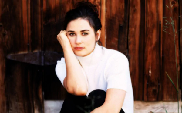 HD desktop wallpaper featuring American actress and celebrity Demi Moore posing thoughtfully against a rustic wooden background.