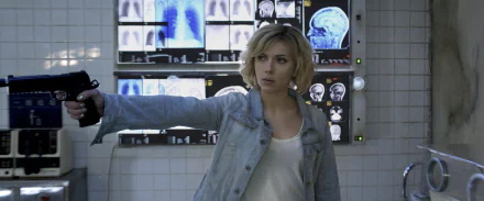 HD desktop wallpaper: blonde woman in a denim jacket aiming a gun in a lab lined with brain scans — scene from the movie Lucy.