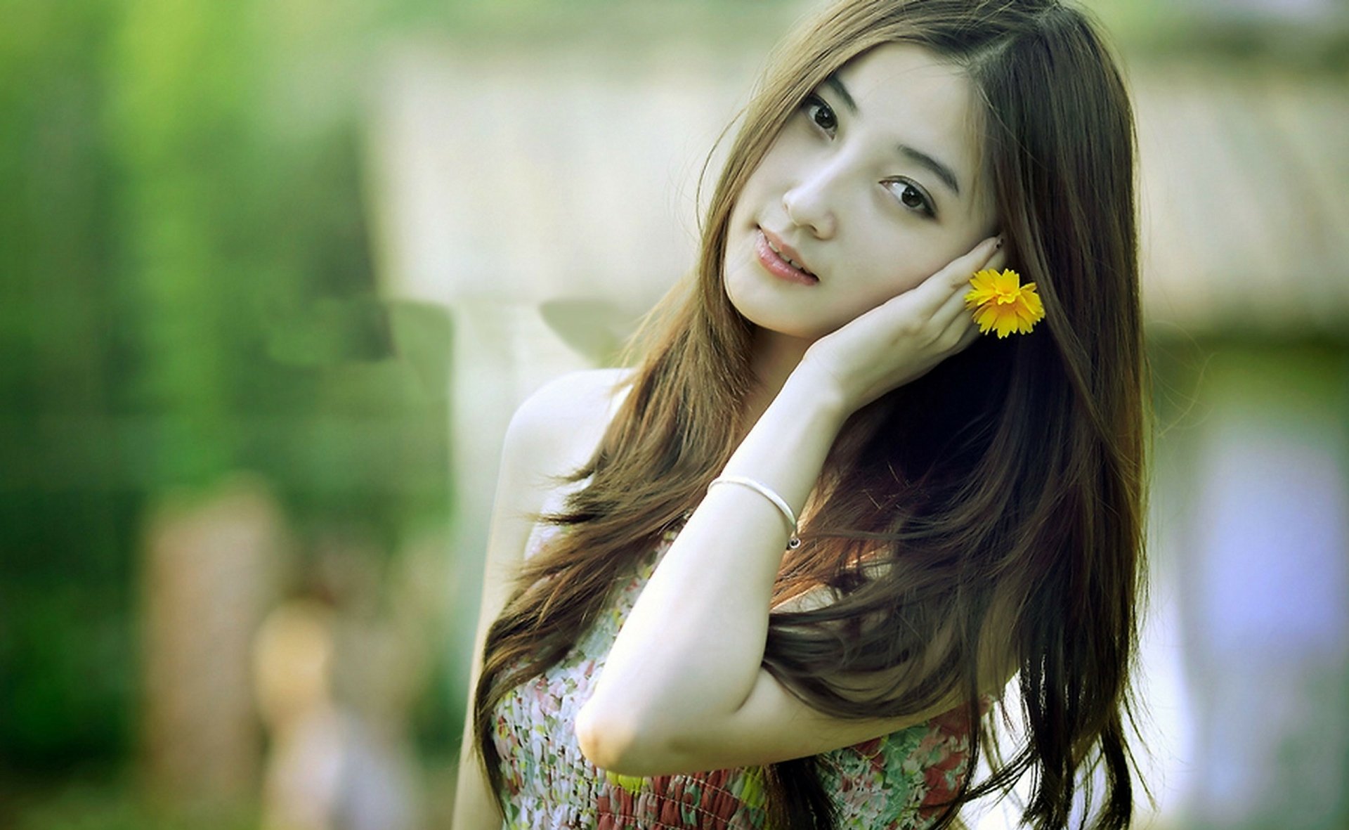 HD desktop wallpaper featuring an Asian woman with long hair, holding a yellow flower near her ear, against a soft-focus outdoor background.