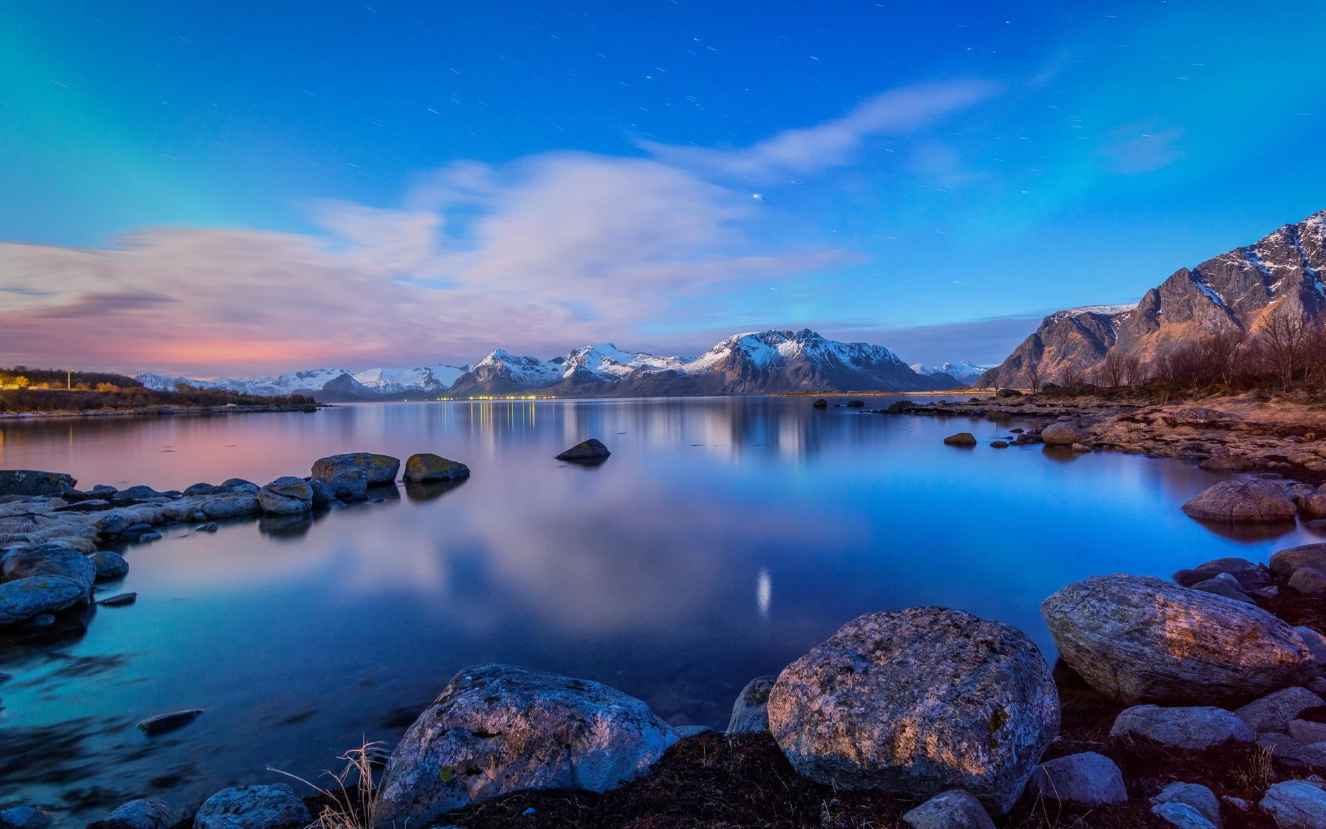 A serene night landscape featuring a tranquil lake reflecting the sky and mountains, surrounded by clouds and rocks, creating a stunning HD desktop wallpaper.