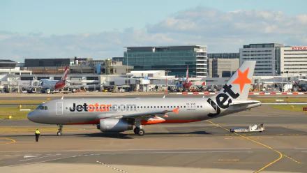 A Jetstar Airbus A320 taxiing at an airport, surrounded by modern terminal buildings and other aircraft, captured in high-definition for a striking desktop wallpaper.